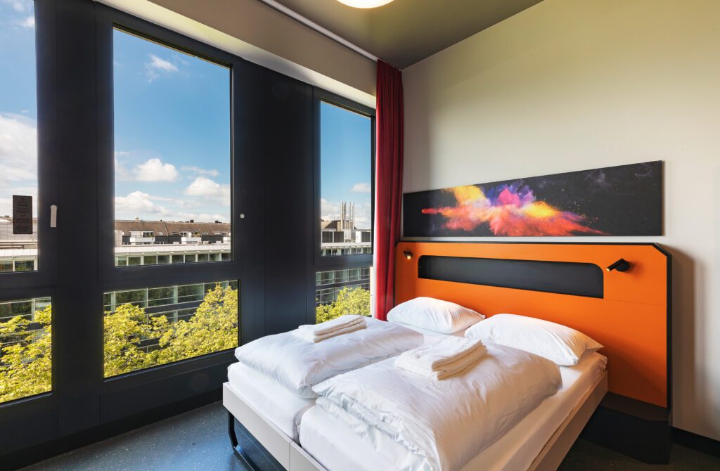MEININGER Hotel Genève Centre Charmilles: Modernes Doppelzimmer mit großen Fenstern und orangefarbenem Design